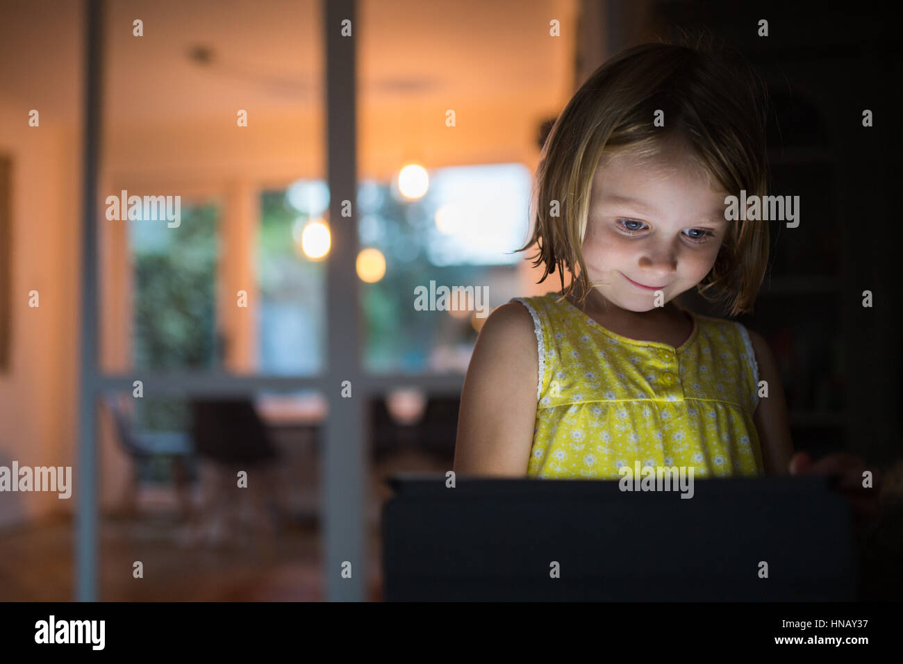 6 anno vecchia ragazza su tablet in serata a casa con la luce che riflette sul suo viso Foto Stock
