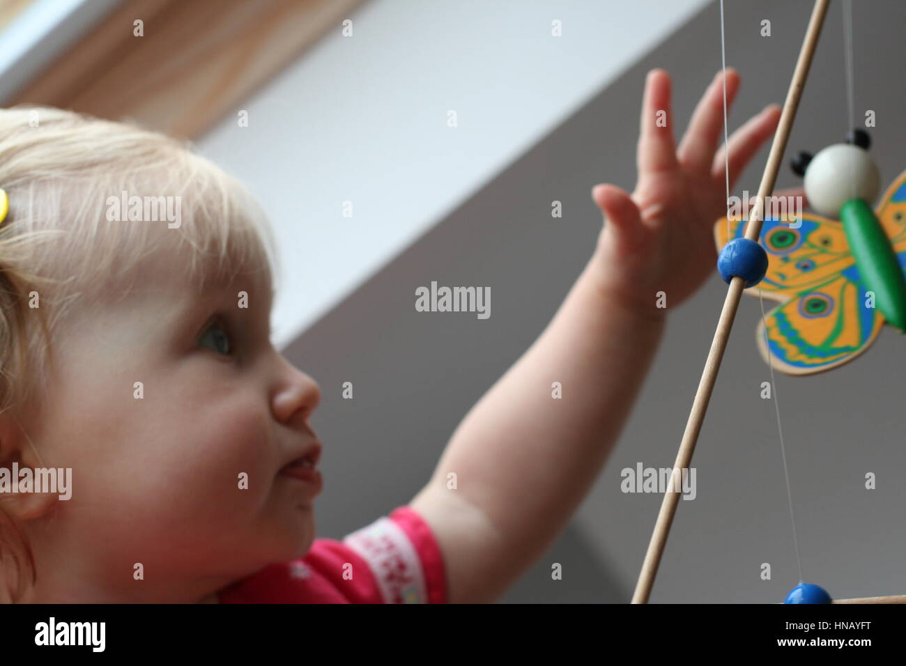La bionda bambina bambino kid giocando con una farfalla in legno culla mobile, lo sviluppo di destrezza e la scoperta di esplorare il concetto di apprendimento esplorare Foto Stock