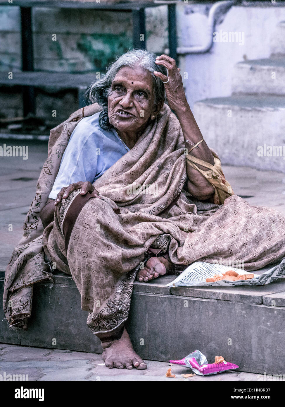 Madurai, India - 19 Ottobre 2013: un vecchio ingrigimento lady si siede sul marciapiede della strada intorno al Tempio di Madurai. Ella ha un espressivo licenziamento fa Foto Stock