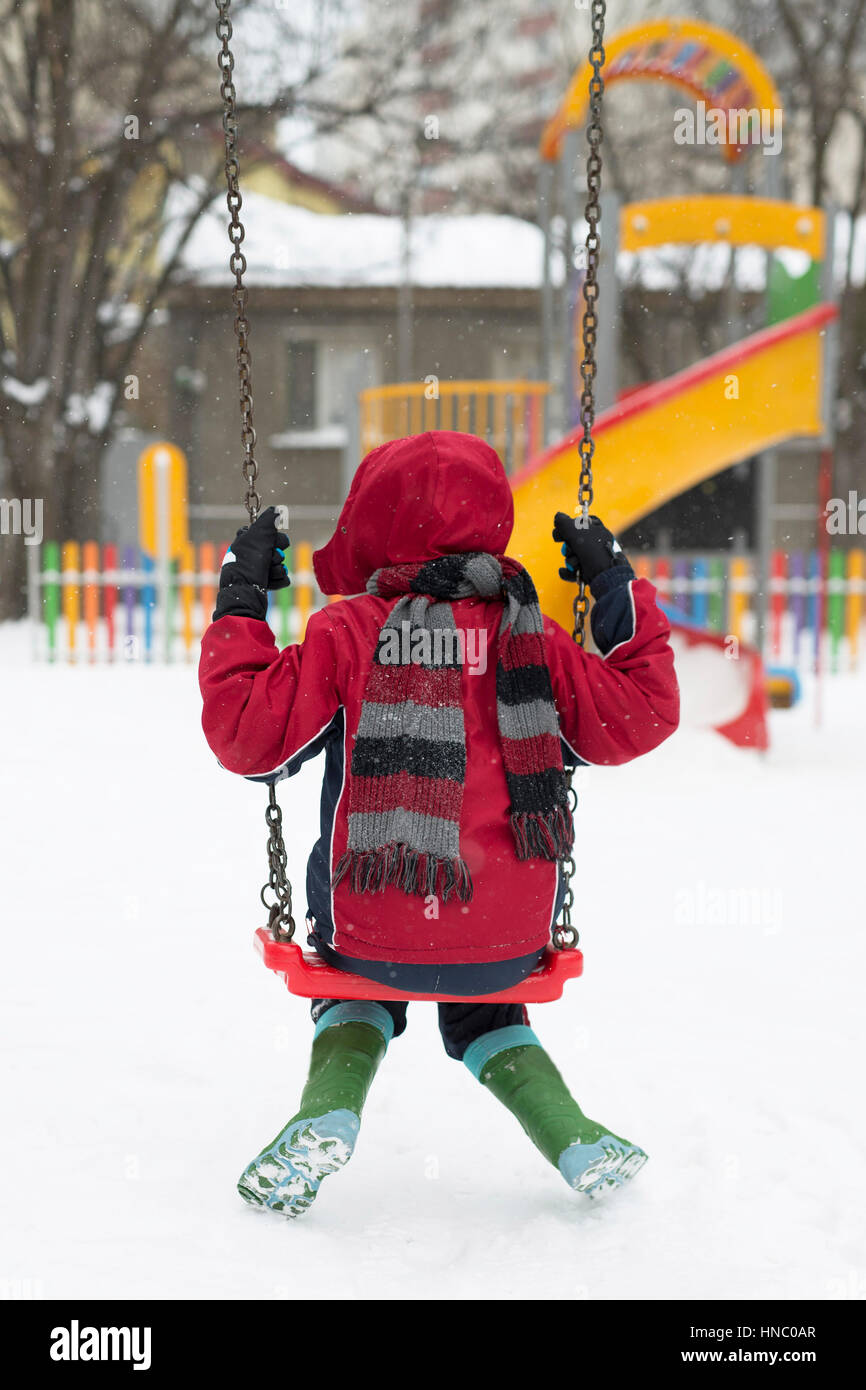Ragazzo seduto su una oscillazione in snow Foto Stock