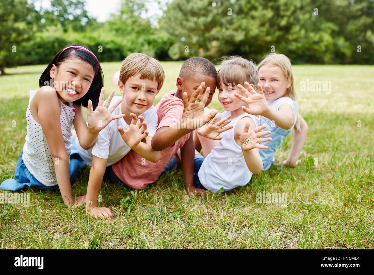 I bambini da scuola materna internazionale seduti sul prato felicemente sventolando Foto Stock