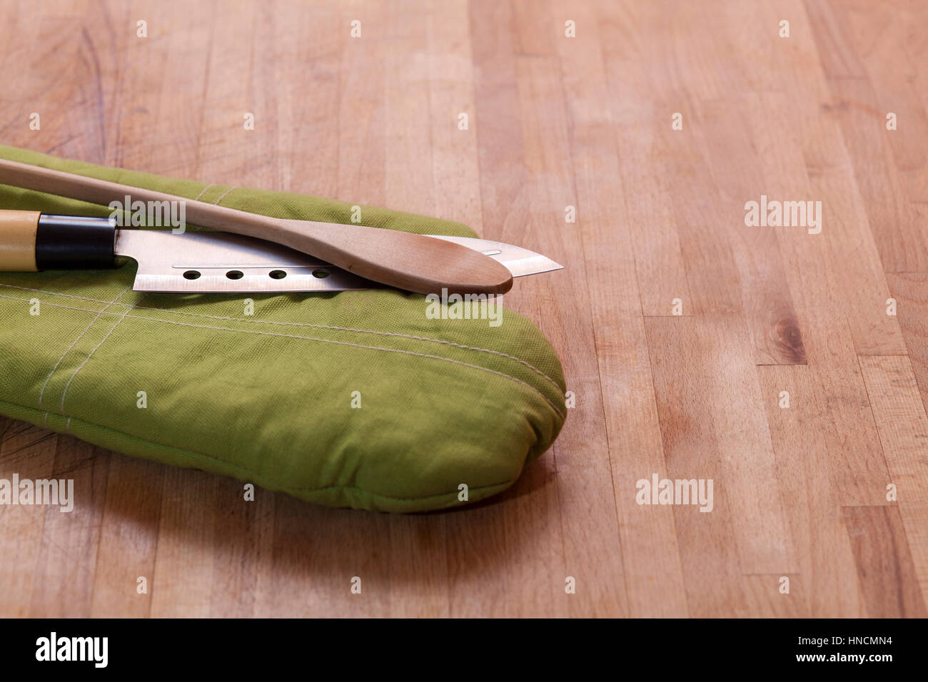 Guanto da forno con un cucchiaio e un coltello su una tavola di legno Foto Stock
