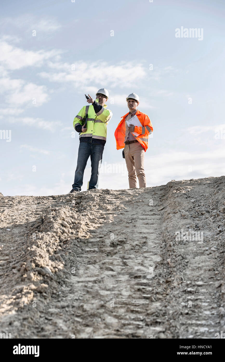 Basso angolo di visione dell'architetto mostrando qualcosa da un collega sul sito in costruzione contro sky Foto Stock