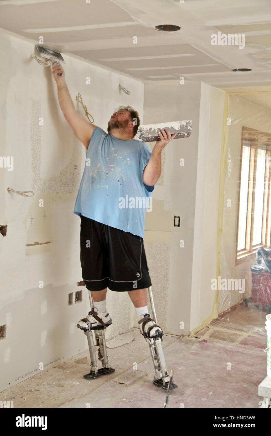 Un muro a secco di finisher spumanti si applica il composto per giunti a soffitto mentre in piedi su palafitte. Foto Stock