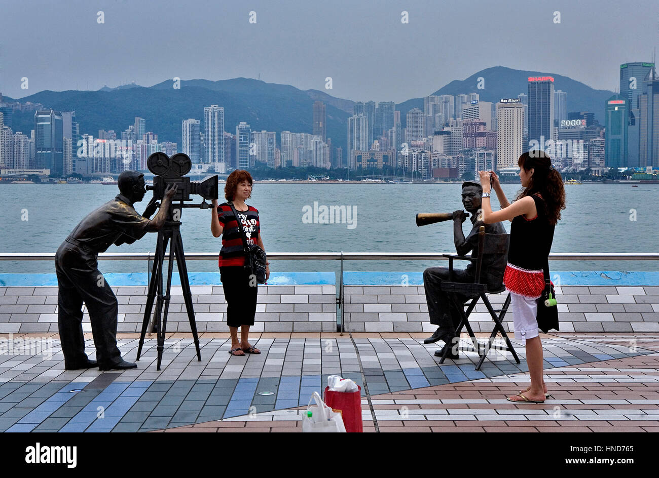 I turisti in Viale delle Stelle. Cameraman e direttore statue con il Victoria Harbour in background,Hong Kong, Cina Foto Stock