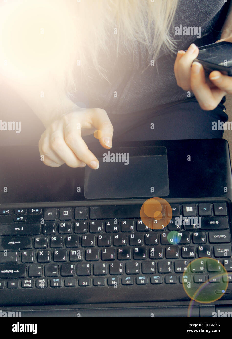 La giovane ragazza dietro il laptop nelle mani del telefono mobile, effetto luce soffusa Foto Stock