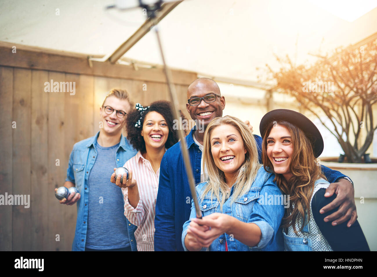 Cinque amici giovani uomini e donne che assumono selfie con selfie stick holding petanque sfere metalliche in mani, sorridente e guardando in alto Foto Stock