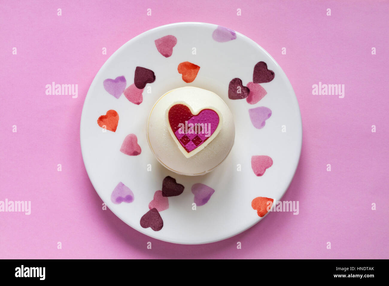 Guardando verso il basso sulla M&S Lampone e sfere di Prosecco per dessert per il giorno di San Valentino sul piatto decorativo con cuori impostato su sfondo rosa Foto Stock