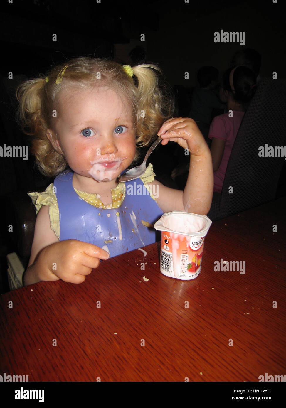 La bionda bambina bambino bambino neonato con parentesi pigtail con yogurt cibo in tutto il suo volto Foto Stock