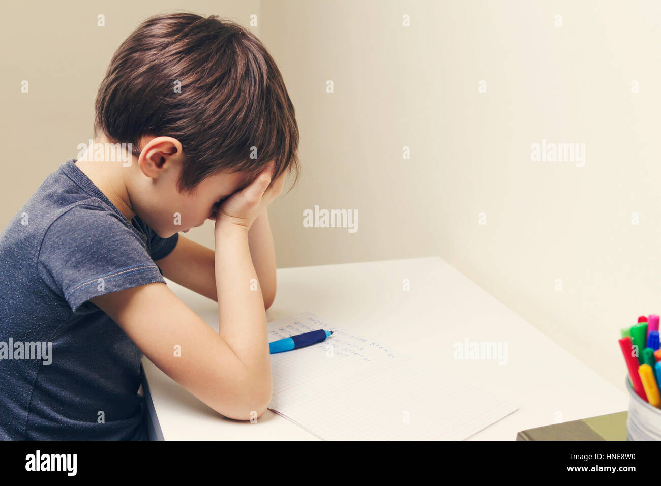 Stanco bambino facendo i compiti a casa. Il ragazzo stufi e si copre il viso con le mani. Istruzione, scuola, difficoltà di apprendimento concetto Foto Stock