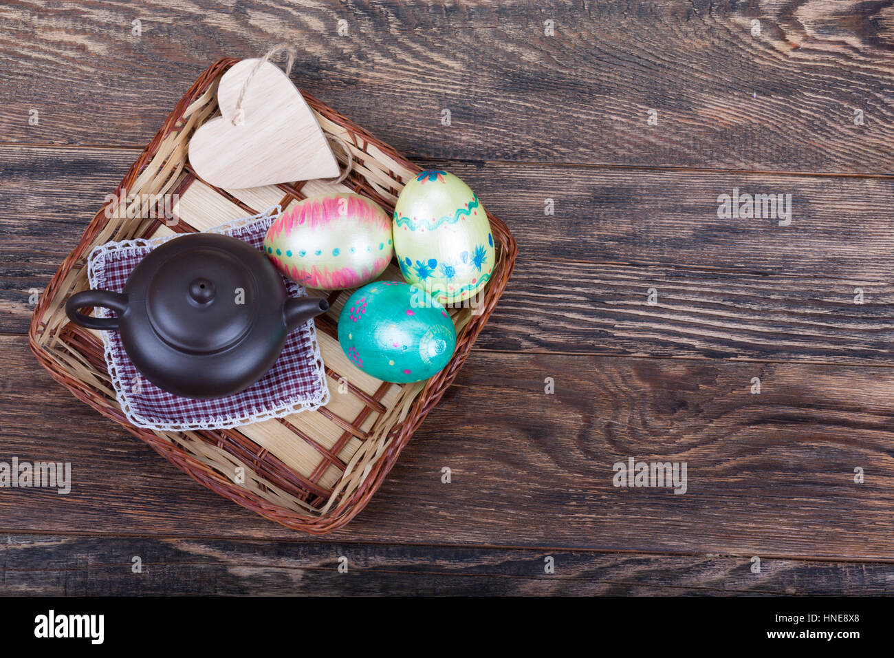 Decorazioni colorate le uova di pasqua con cuore di legno sagomato e teiera su sfondo di legno Foto Stock