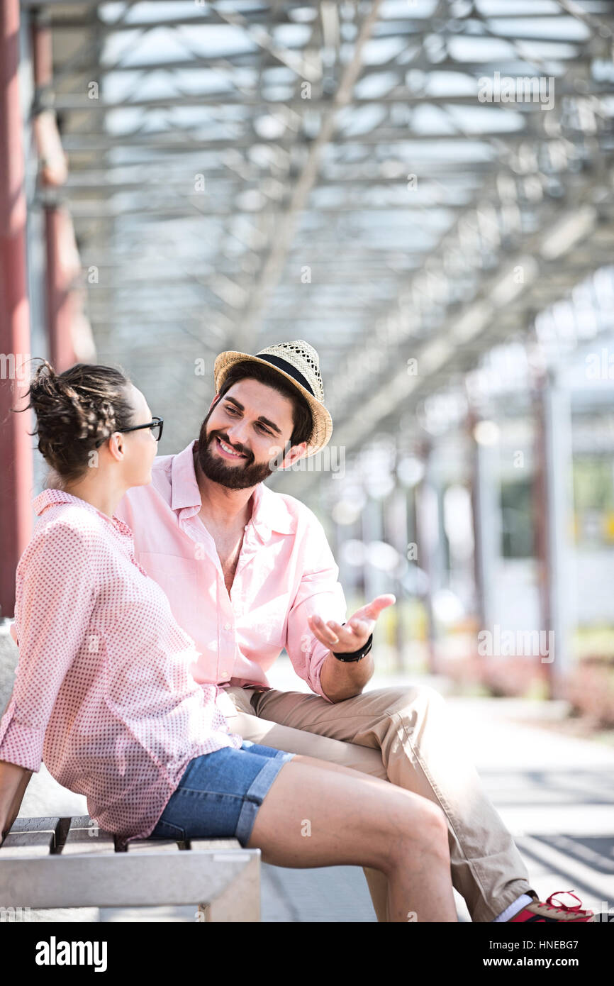 Felice l'uomo a parlare con una donna durante la seduta sul banco sotto ombra Foto Stock