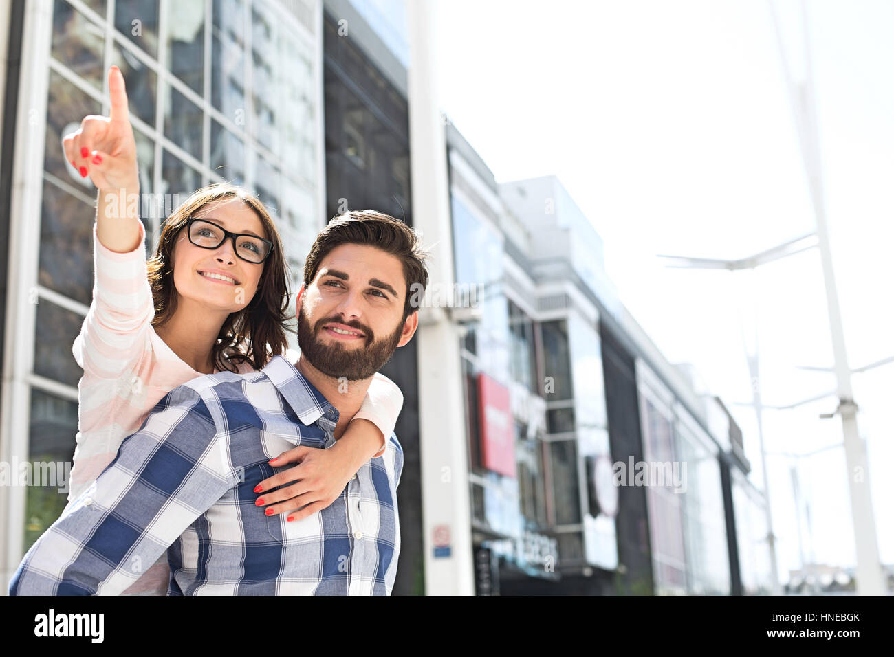 Donna sorridente rivolto lontano mentre godendo piggyback ride su uomo in città Foto Stock