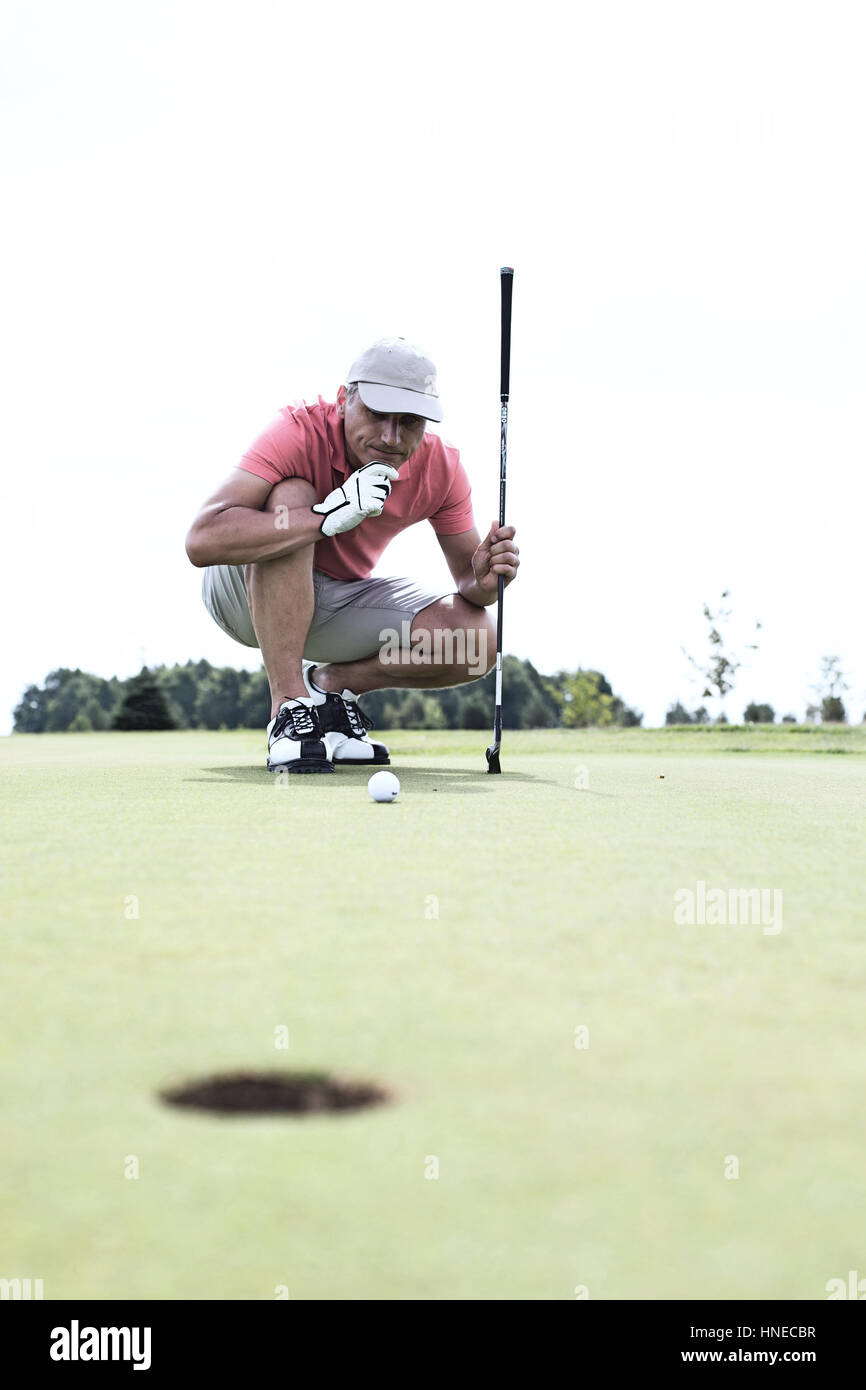Uomo di mezza età guardando a sfera mentre accovacciato sul campo da golf Foto Stock