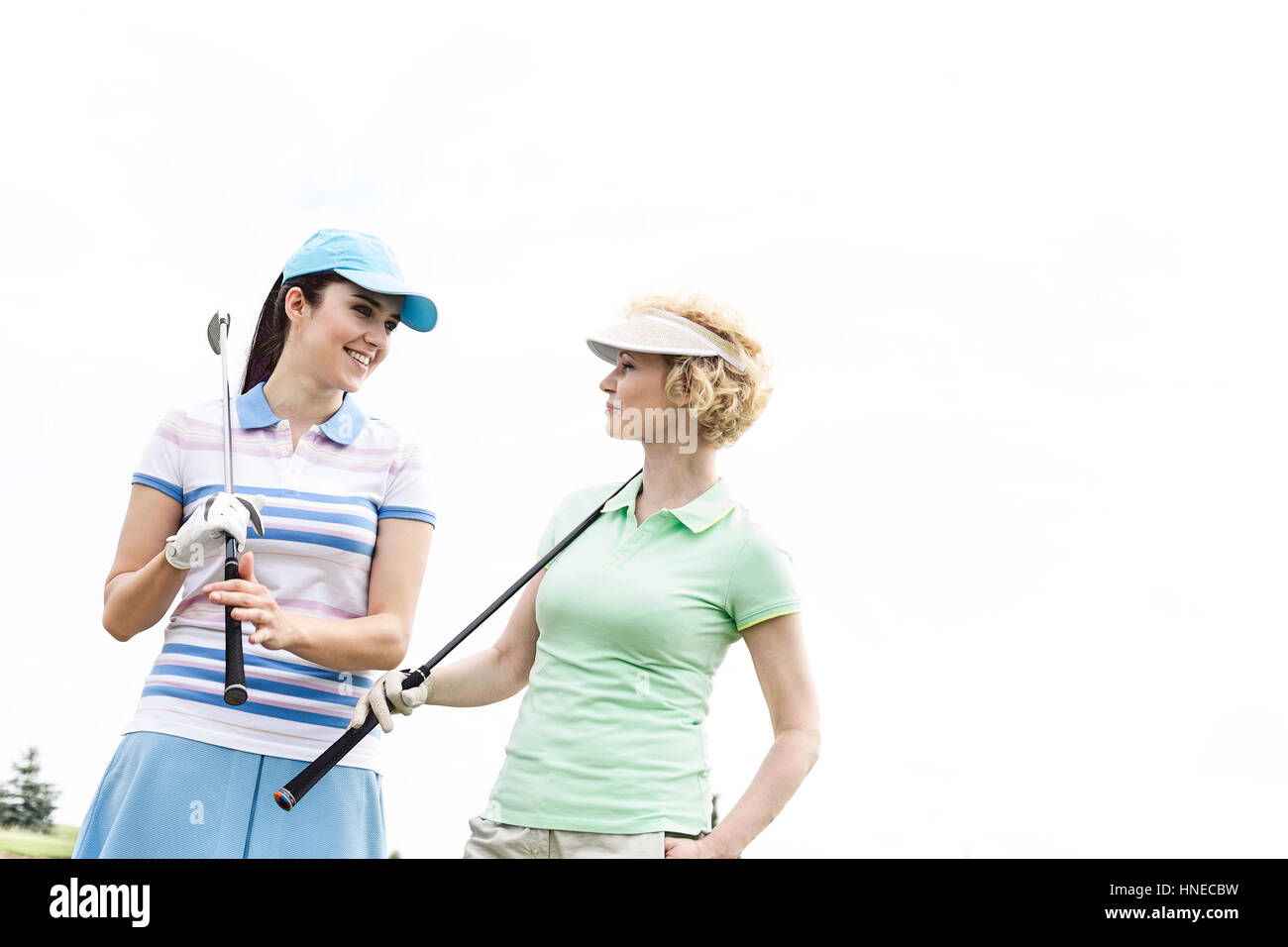 Felice golfisti femmina guardando ogni altro contro il cielo chiaro Foto Stock
