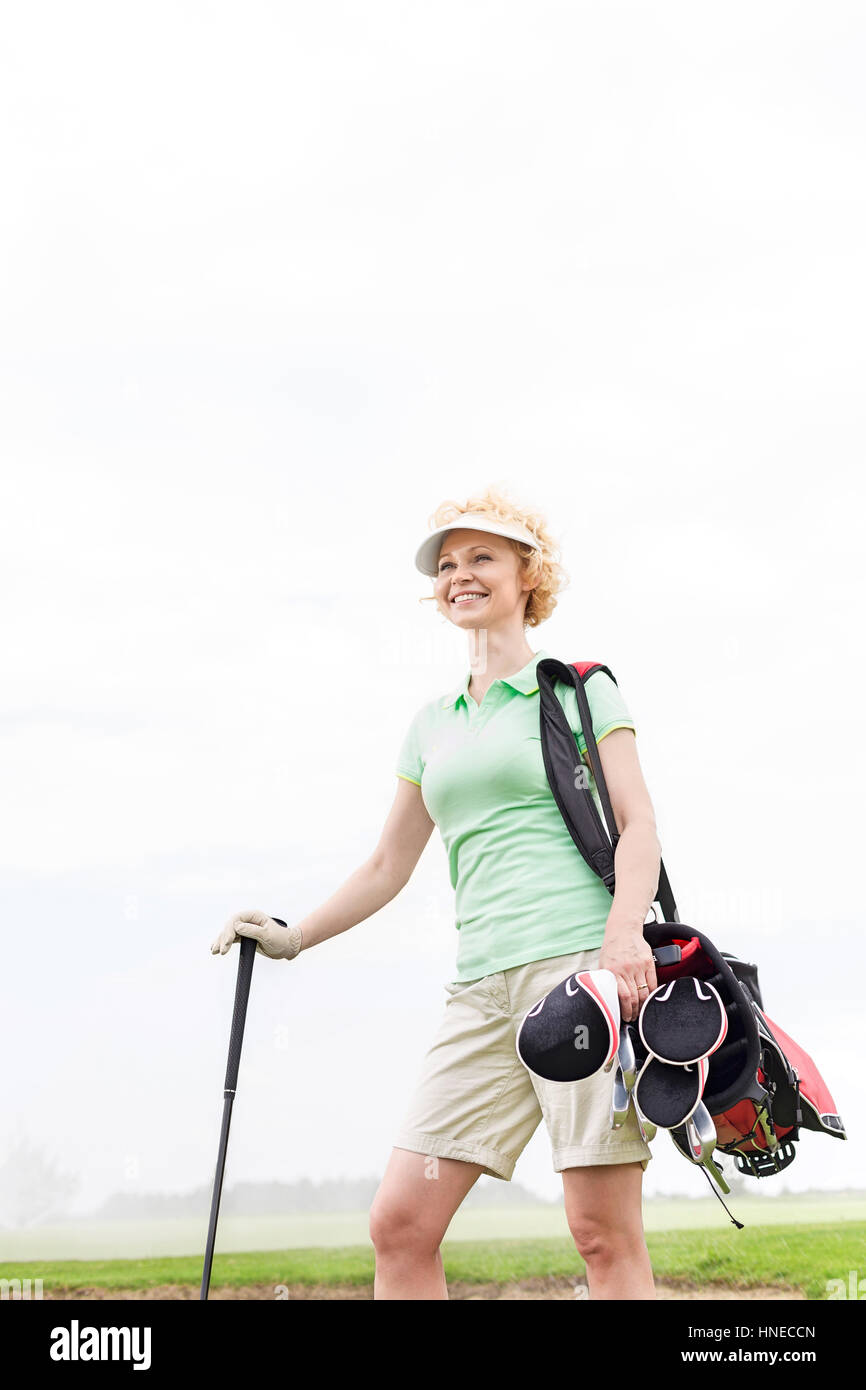 Basso angolo di vista sorridente golfista femmina in piedi contro il cielo chiaro Foto Stock