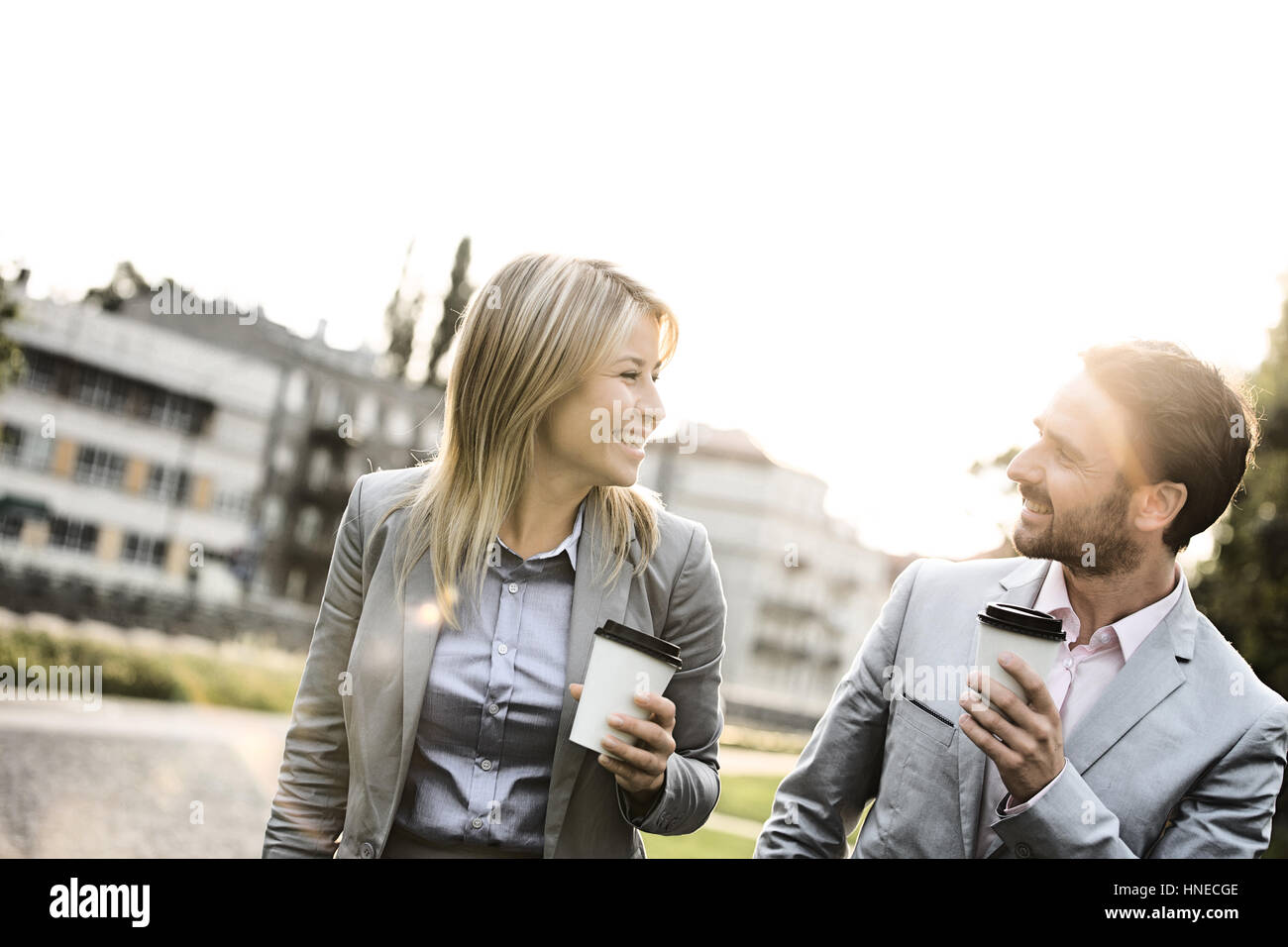 Happy business giovane conversare mentre si tiene tazze monouso in città Foto Stock