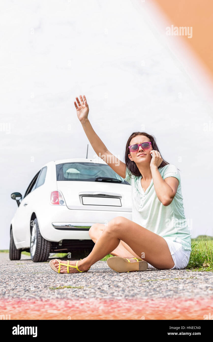 Frustrati donna autostop mentre si utilizza il telefono cellulare sulla strada di campagna da ripartiti in auto Foto Stock