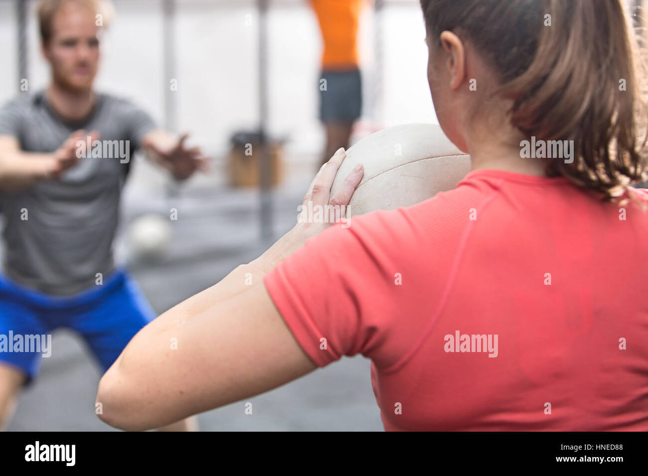 Vista posteriore della donna medicina lanciando la palla verso l'uomo in palestra crossfit Foto Stock
