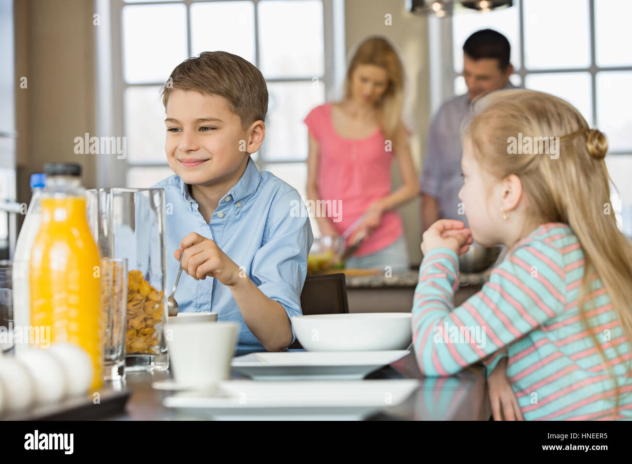 I fratelli aventi la prima colazione al tavolo con i genitori la cottura in background Foto Stock