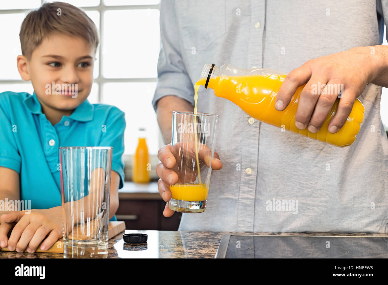 Sezione mediana del padre che serve il succo d'arancia per figlio in cucina Foto Stock
