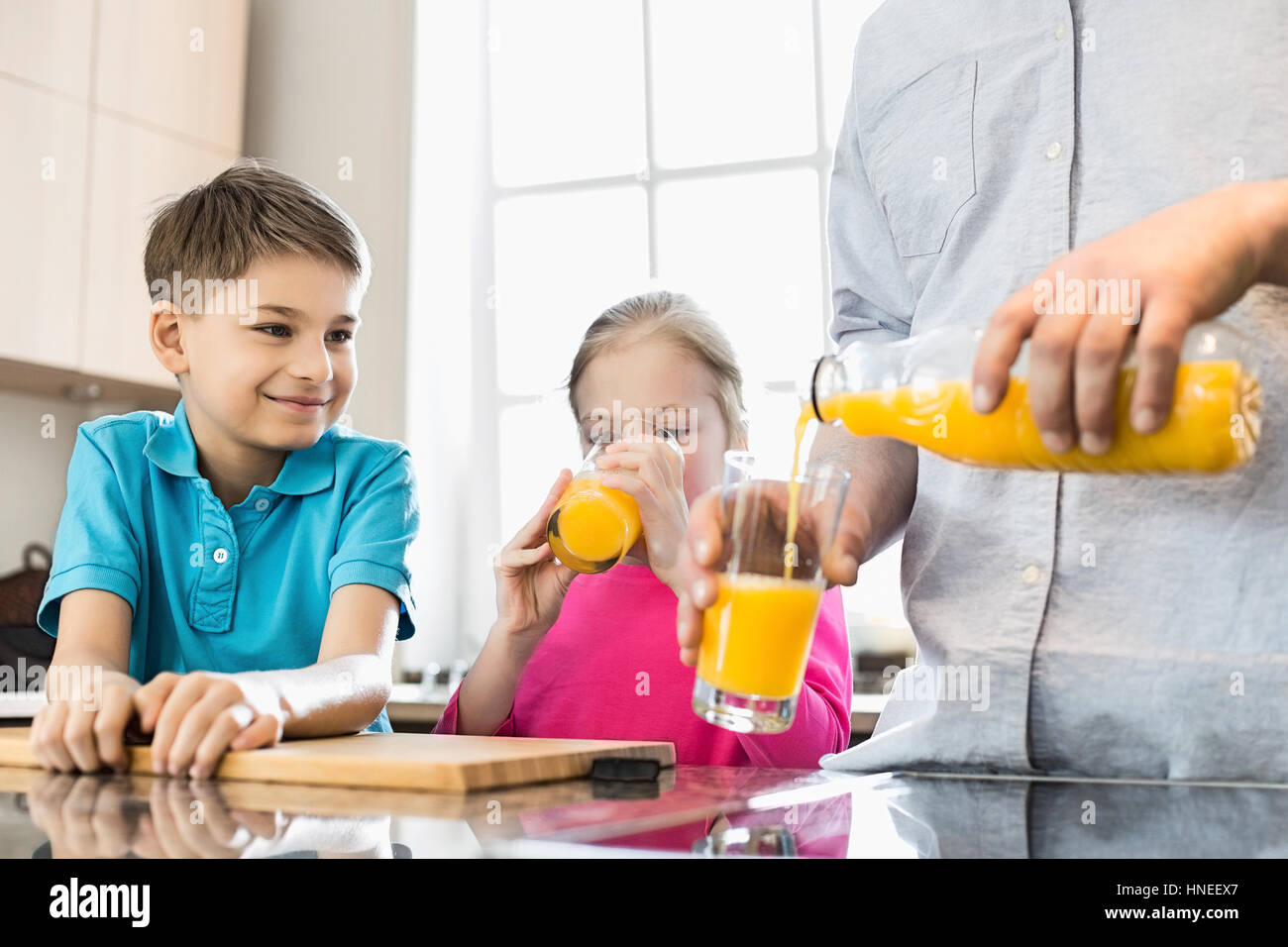 Sezione mediana del padre che serve il succo d'arancia per i bambini in cucina Foto Stock
