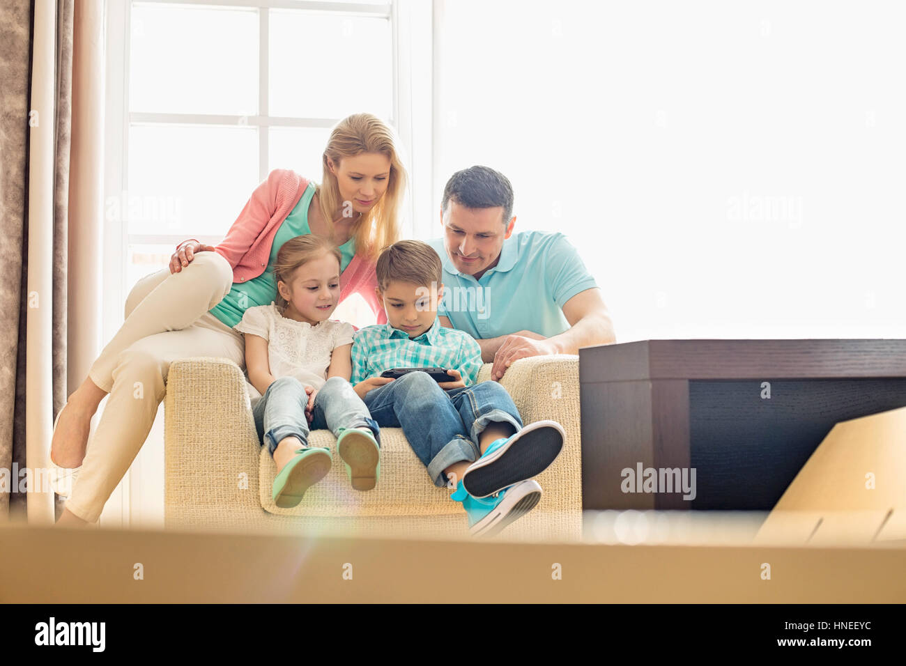 Famiglia guardando il ragazzo giocando hand-held video gioco a casa Foto Stock