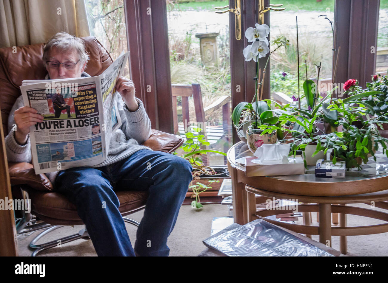 Un uomo si siede in una comoda poltrona leggendo il quotidiano Daily Mail. Foto Stock