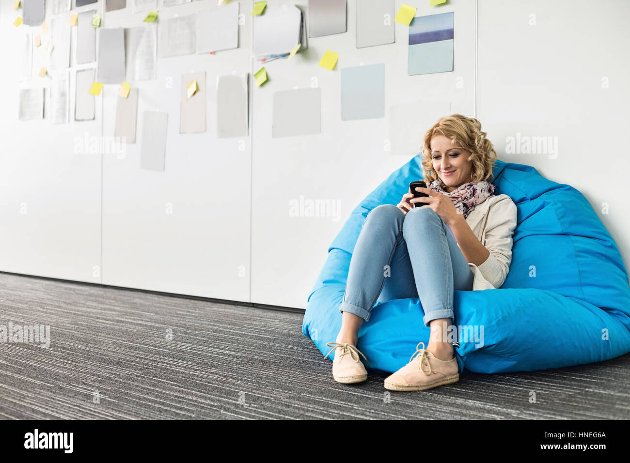 Sorridente imprenditrice utilizzando il telefono cellulare sulla sedia beanbag nel creative office Foto Stock