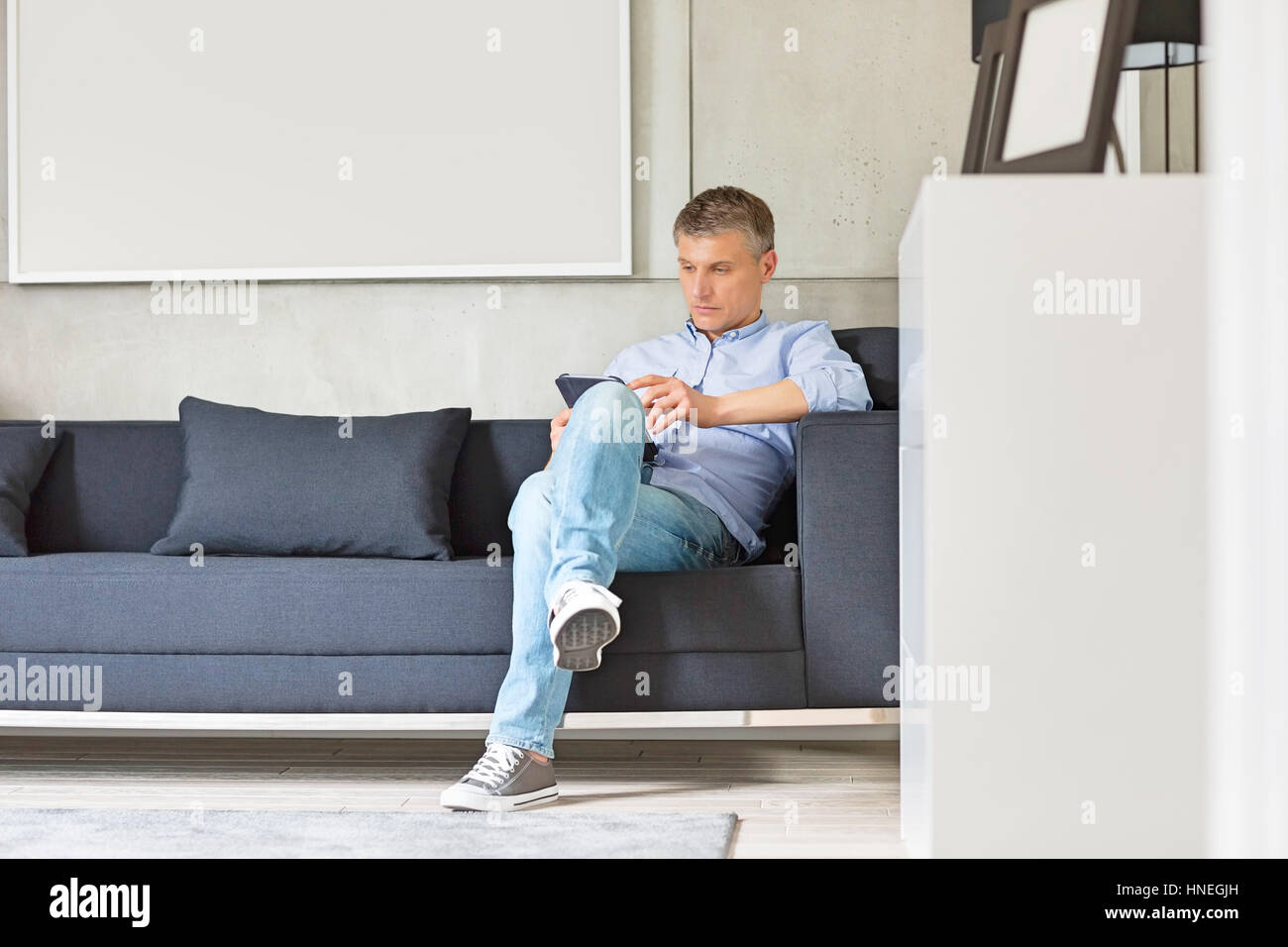 Lunghezza intera di uomo di mezza età con tavoletta digitale sul divano Foto Stock