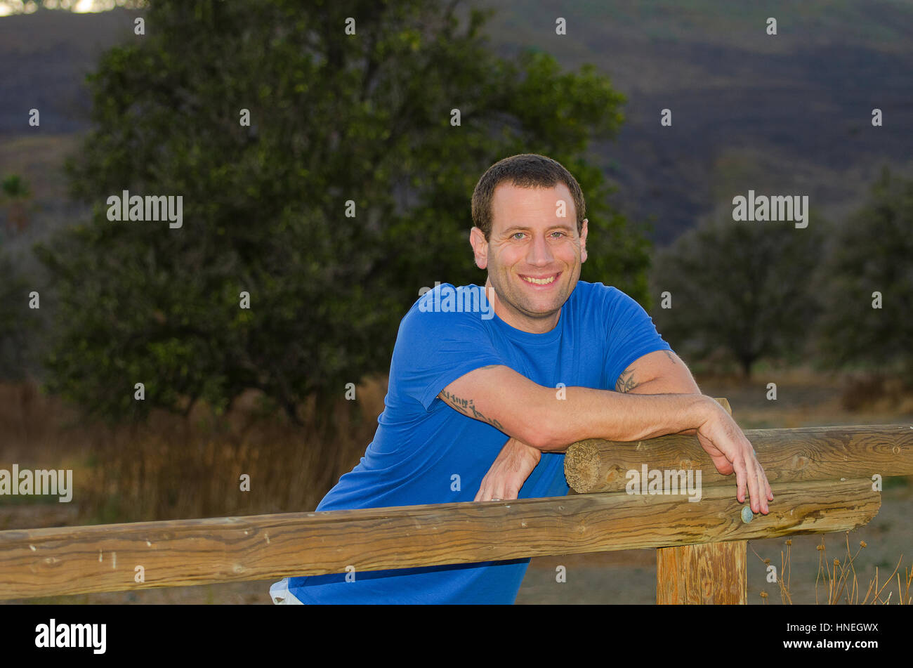 Uomo sorridente appoggiato su di una recinzione di legno godendo la vita all'aperto Foto Stock