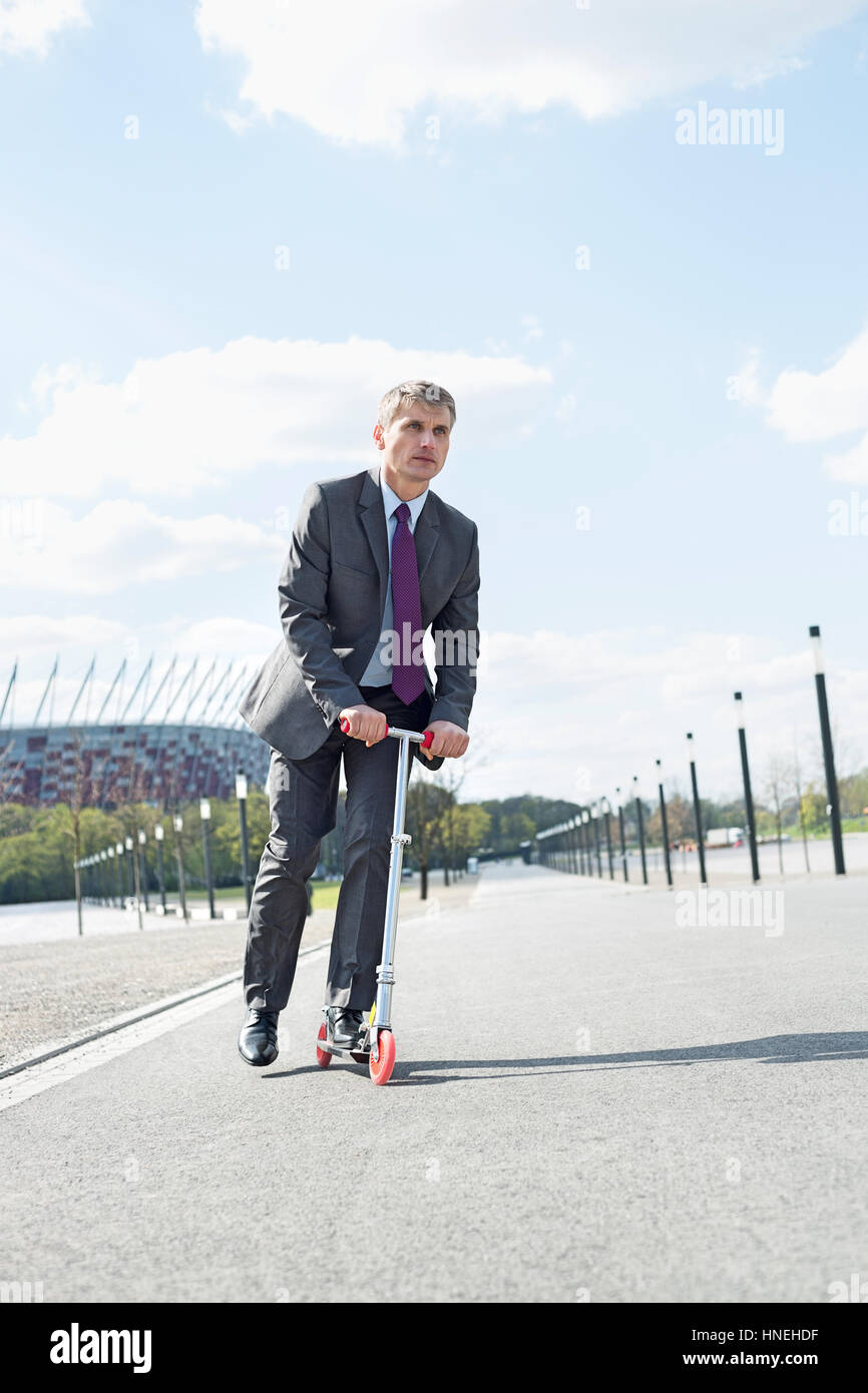 Imprenditore che guarda lontano mentre cavalcate scooter su strada Foto Stock