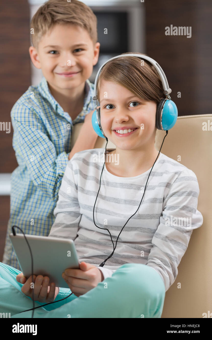 Ritratto di ragazza carina ascoltando musica su tavoletta digitale mentre il fratello in piedi dietro di lei Foto Stock