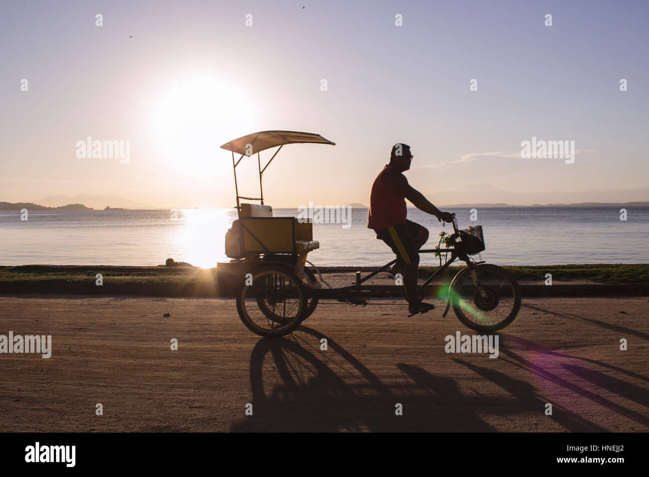 Il Brasile, Stato di Rio de Janeiro, Paqueta Isola, persone in bicicletta sulla costa dell'isola durante il tramonto. Foto Stock