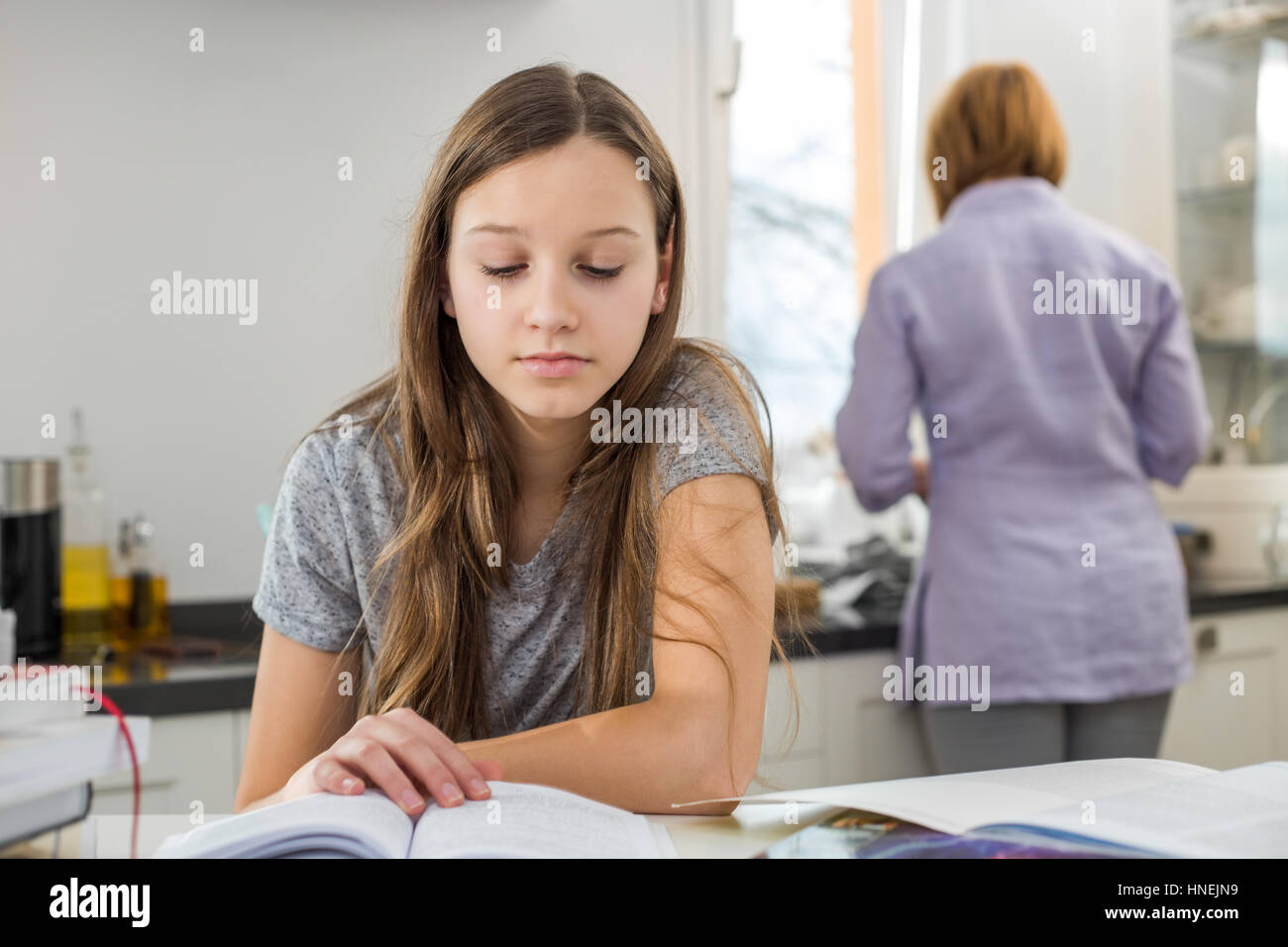 Ragazza che studiano a tavola con la madre in piedi in background Foto Stock