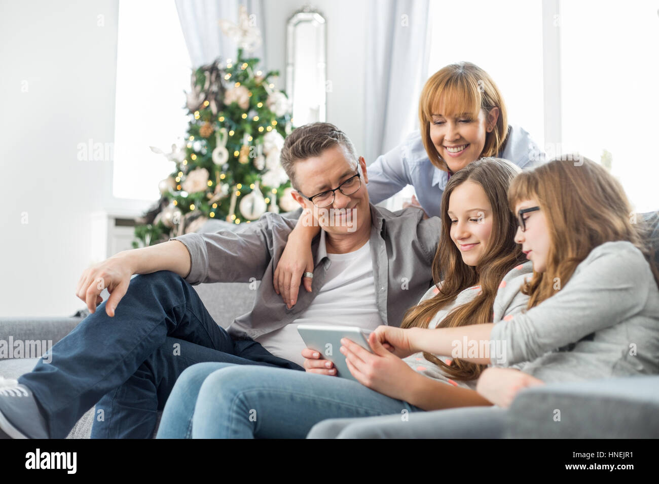 La famiglia tramite tablet PC sul divano con albero di Natale in background Foto Stock