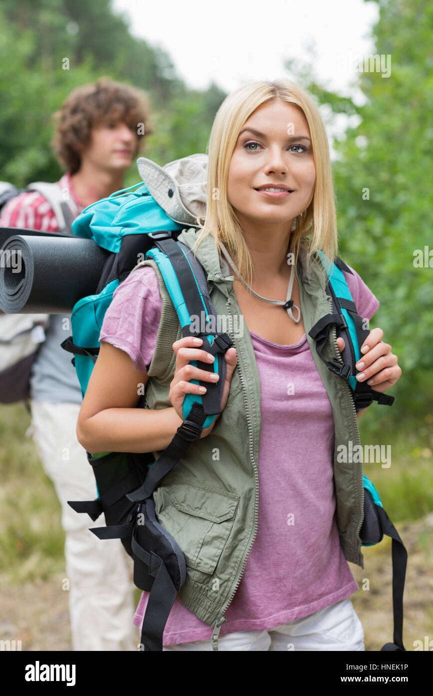 Bellissima femmina backpacker che guarda lontano con uomo in piedi in background in foresta Foto Stock