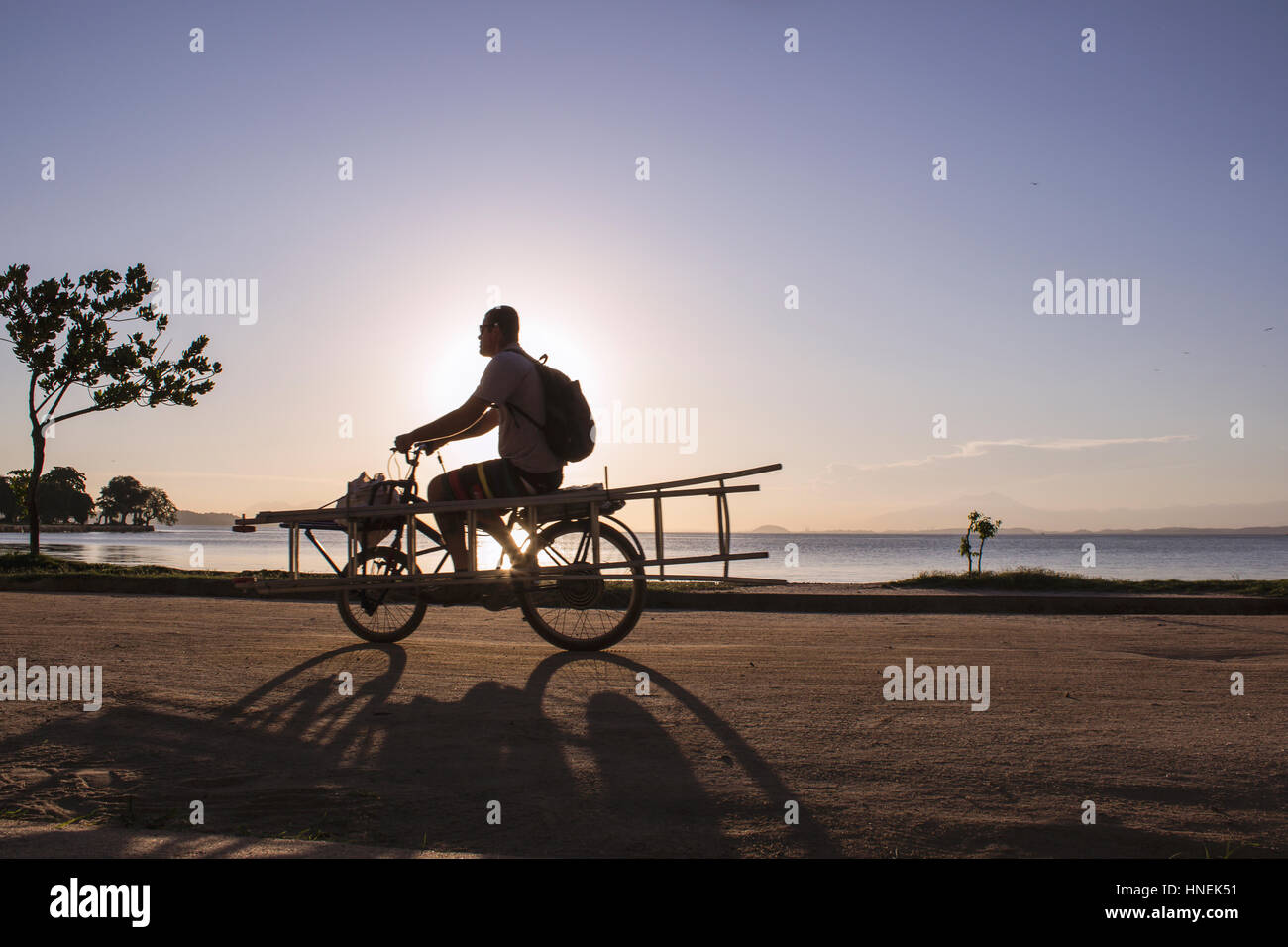 Il Brasile, Stato di Rio de Janeiro, Paqueta Isola, persone in bicicletta sulla costa dell'isola durante il tramonto. Foto Stock