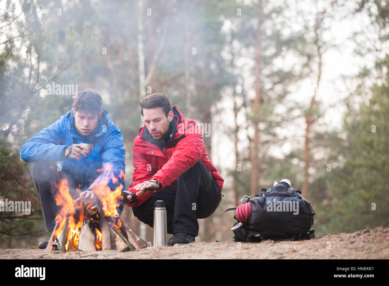 Gli escursionisti maschio mani di riscaldamento a fuoco nella foresta Foto Stock