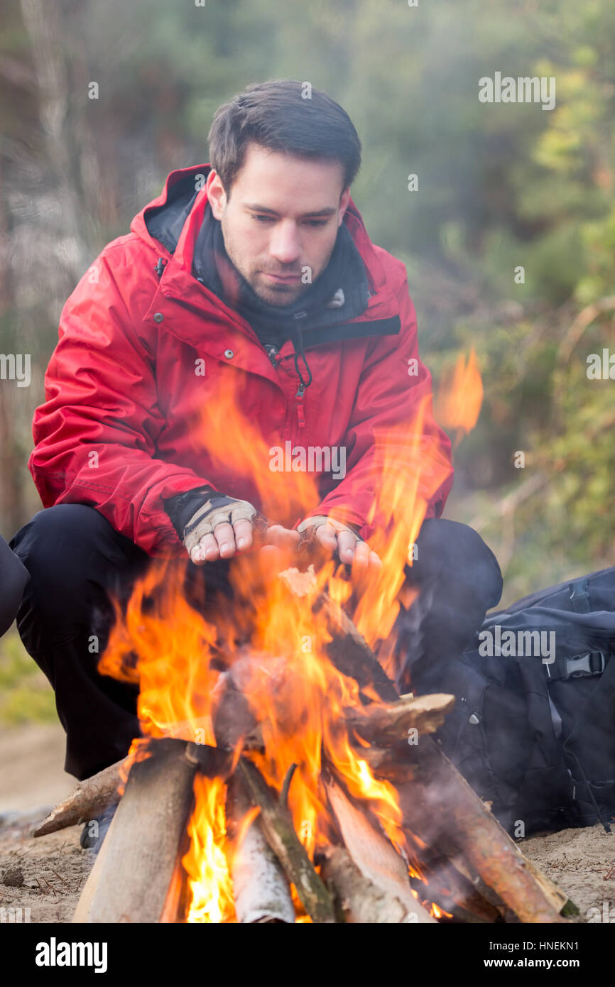 Escursionista maschio riscaldando le mani a fuoco nella foresta Foto Stock