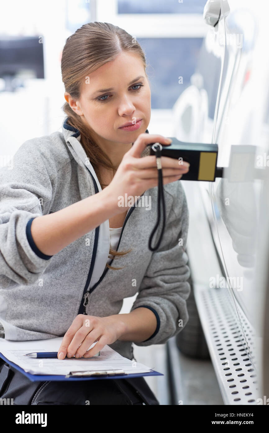 Femmina tecnico di manutenzione controllando la vernice dell'auto con attrezzature di officina Foto Stock