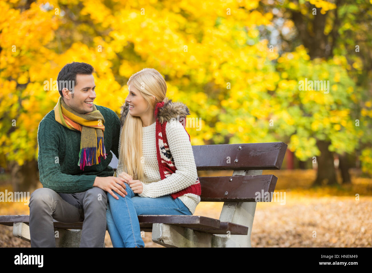 Felice coppia giovane guardando ogni altro mentre è seduto su una panchina nel parco durante l'autunno Foto Stock