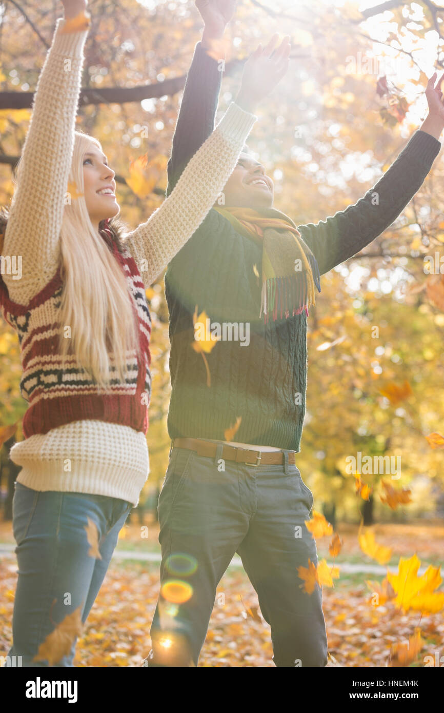 Felice coppia giovane con le braccia sollevate godendo la caduta di foglie di autunno nel parco Foto Stock