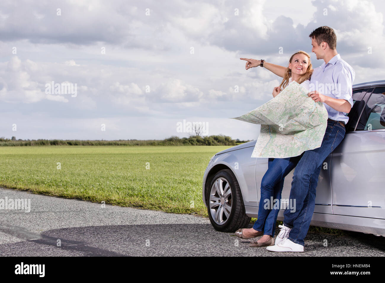 Lunghezza completa di coppia con mappa discutendo di direzione mentre appoggiato su auto in campagna Foto Stock