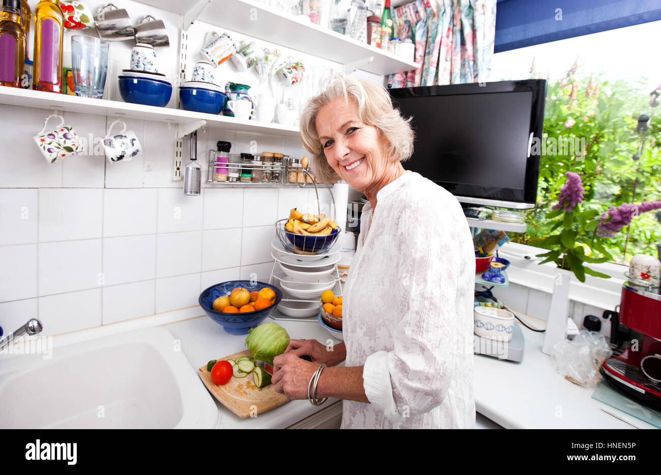 Ritratto di felice donna senior tritare verdure fresche al banco di cucina Foto Stock