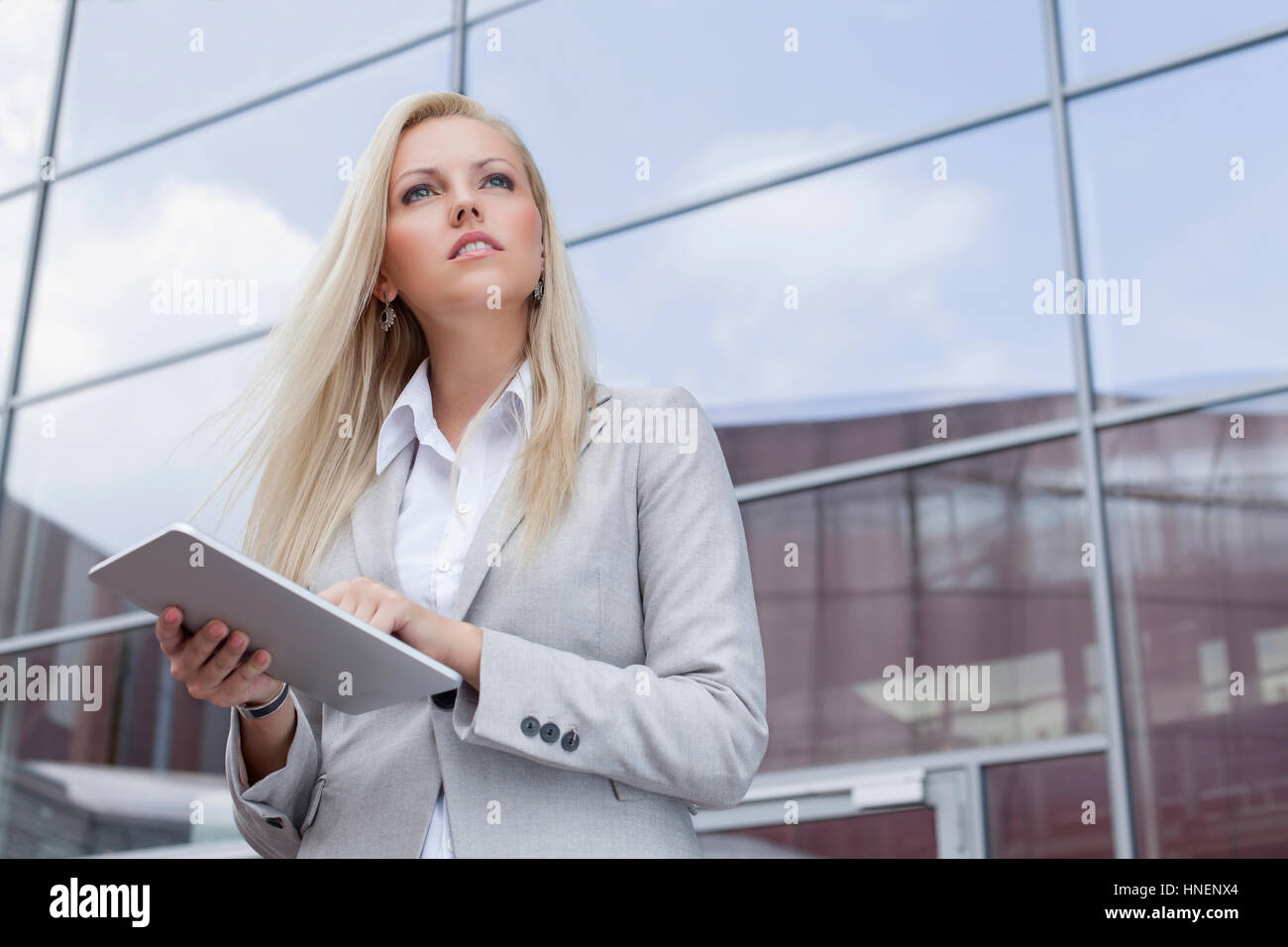 Basso angolo vista di imprenditrice azienda digitale compressa mentre guarda lontano contro l edificio per uffici Foto Stock