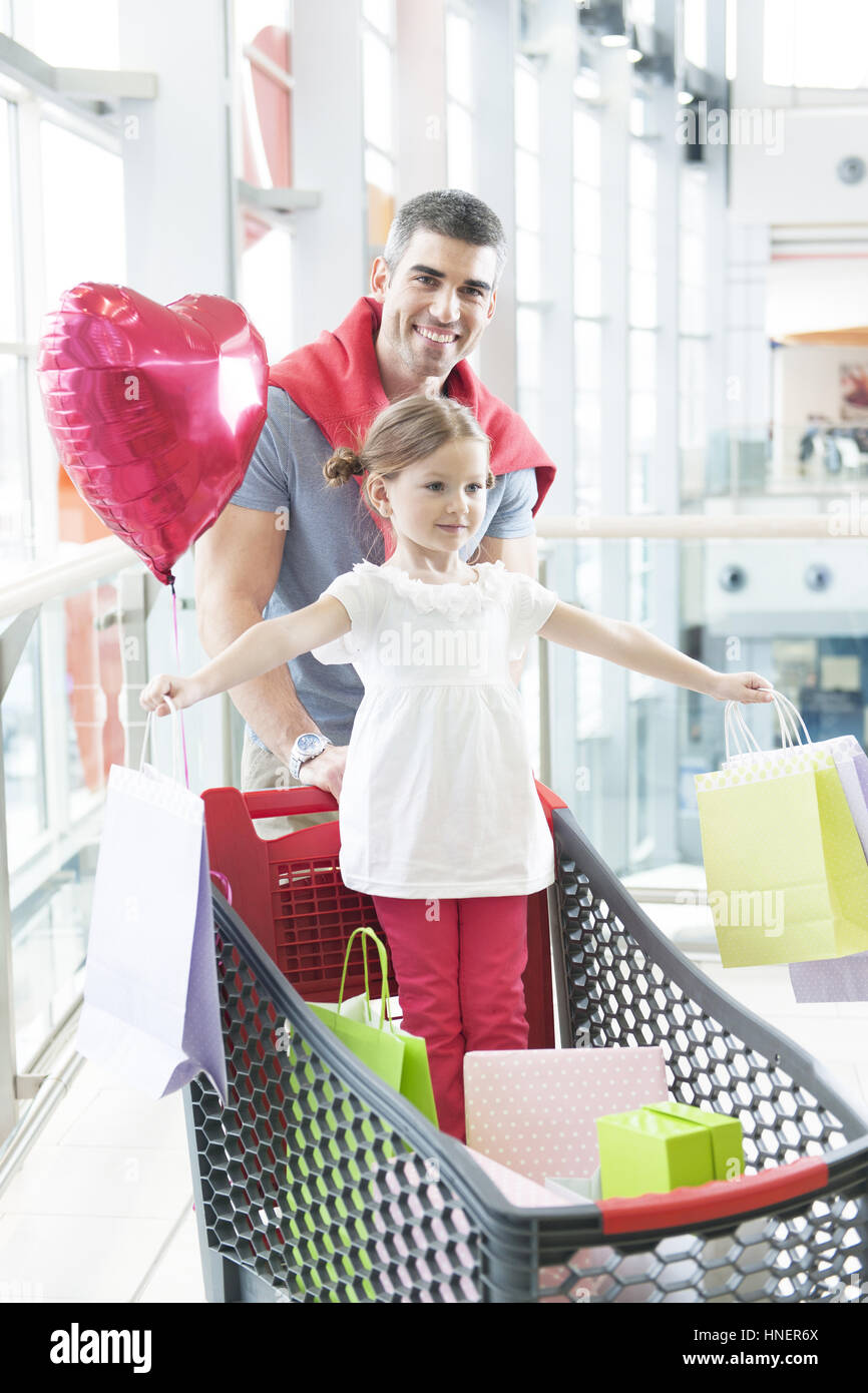 Padre spingendo giovane figlia nel carrello della spesa con borse per lo shopping Foto Stock