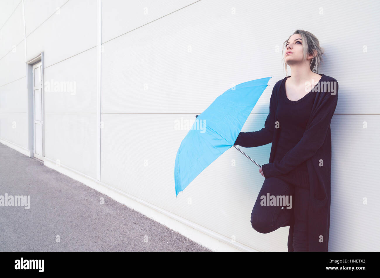 Giovane donna con ombrello blu alla ricerca e attesa per la pioggia Foto Stock