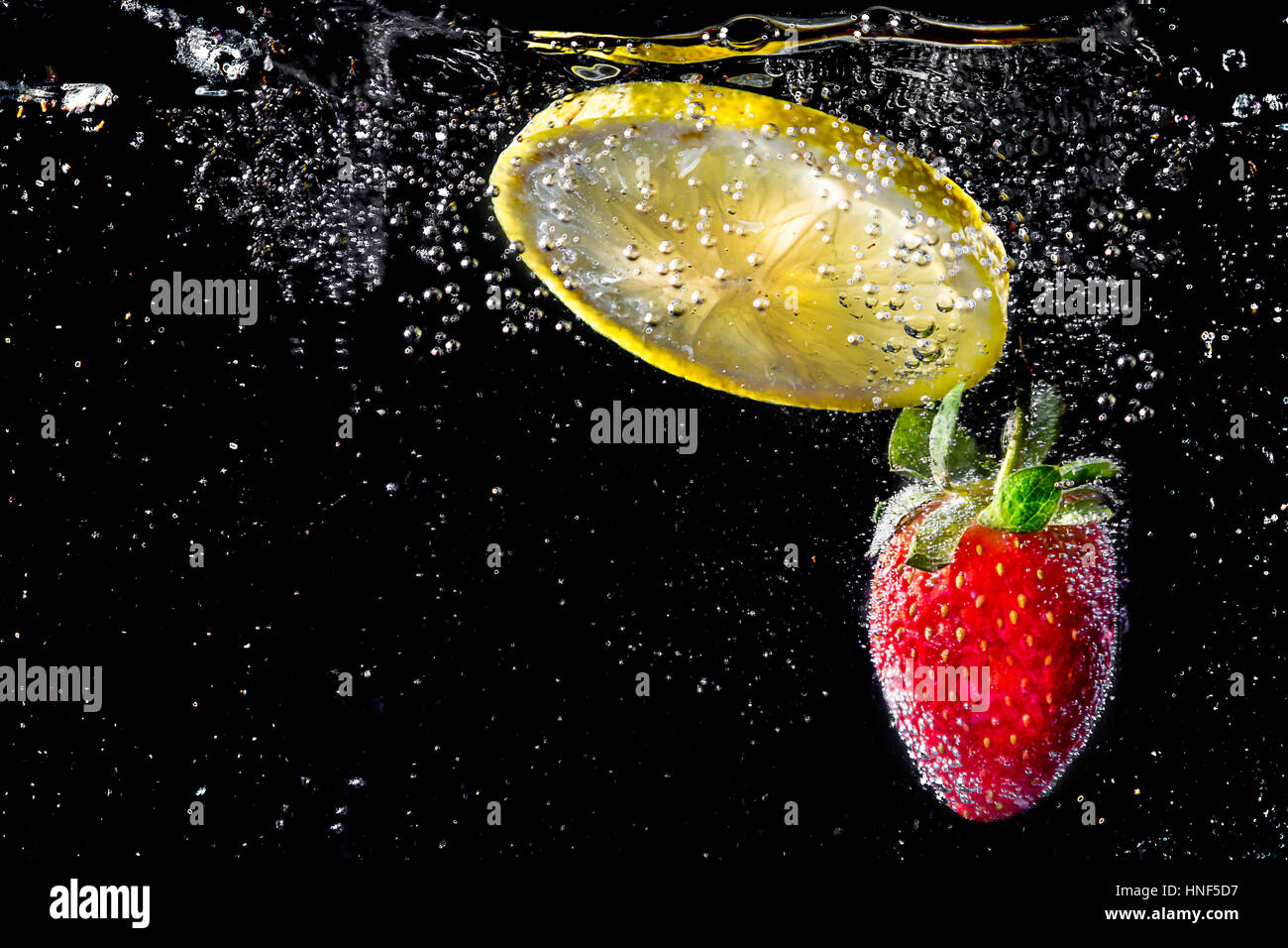 Fettina di limone con fragola cadere in acqua frizzante Foto Stock