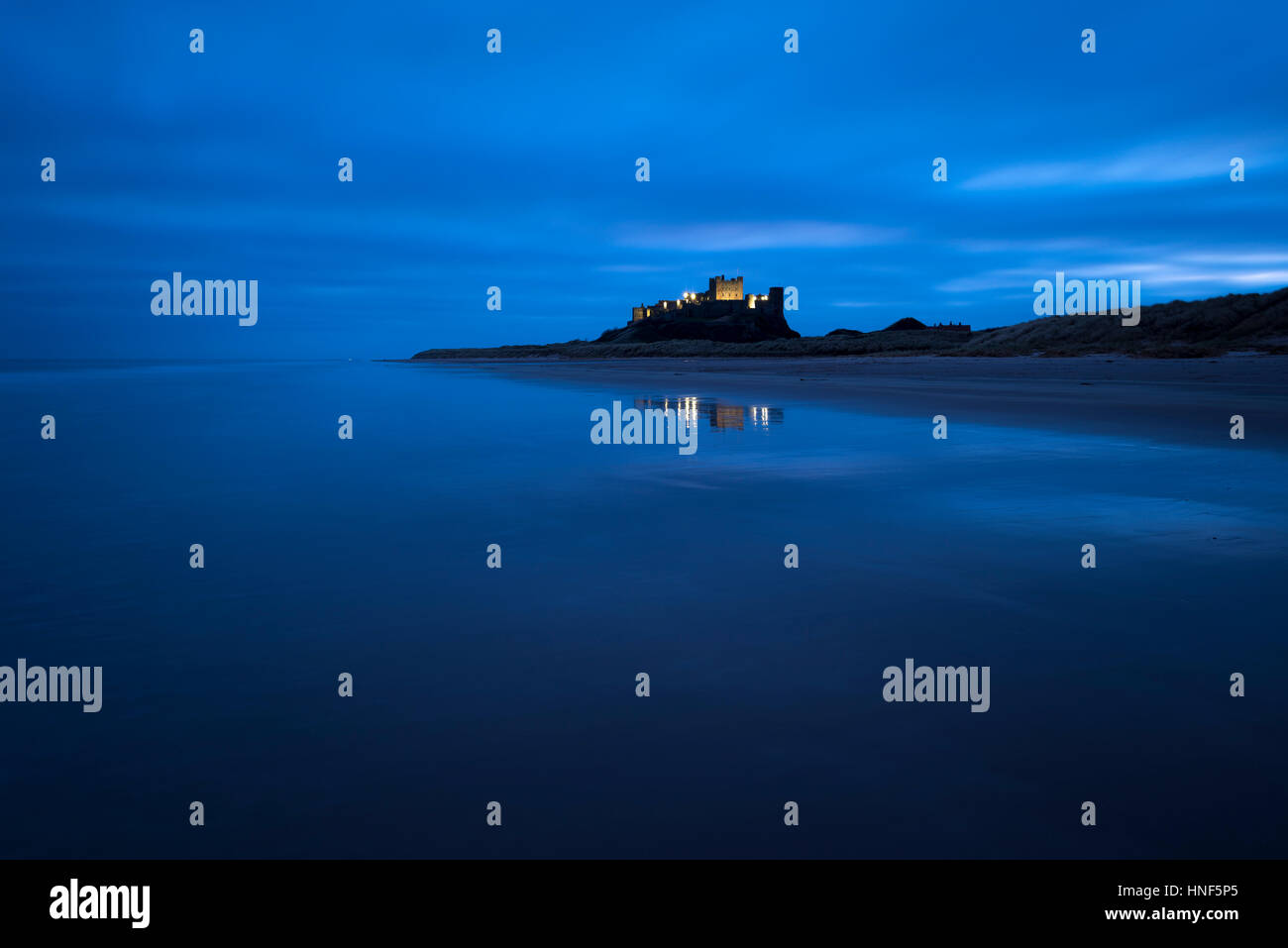 Il castello di Bamburgh illuminato nella pre-alba luce sulla costa di Northumberland. Foto Stock